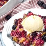 cake mix blackberry cobbler on a small white plate with a scoop of vanilla ice cream and a silver fork on the side