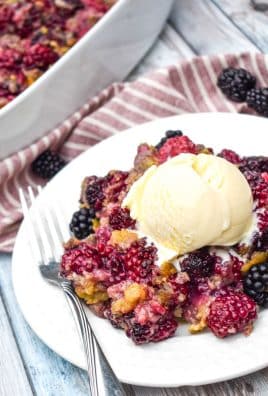 cake mix blackberry cobbler on a small white plate with a scoop of vanilla ice cream and a silver fork on the side