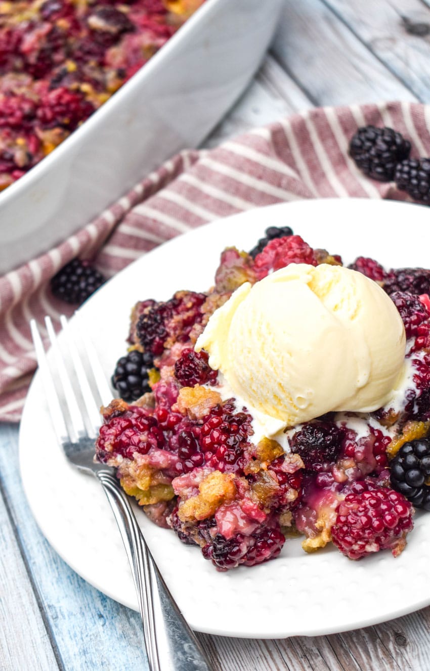 cake mix blackberry cobbler on a small white plate with a scoop of vanilla ice cream and a silver fork on the side