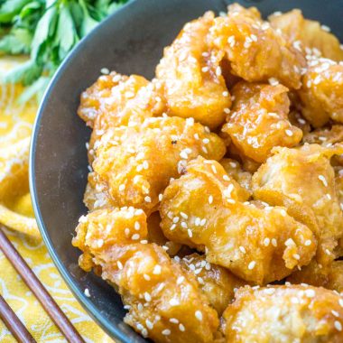 Asian style crispy honey chicken served in a black bowl with fresh green herbs in the background