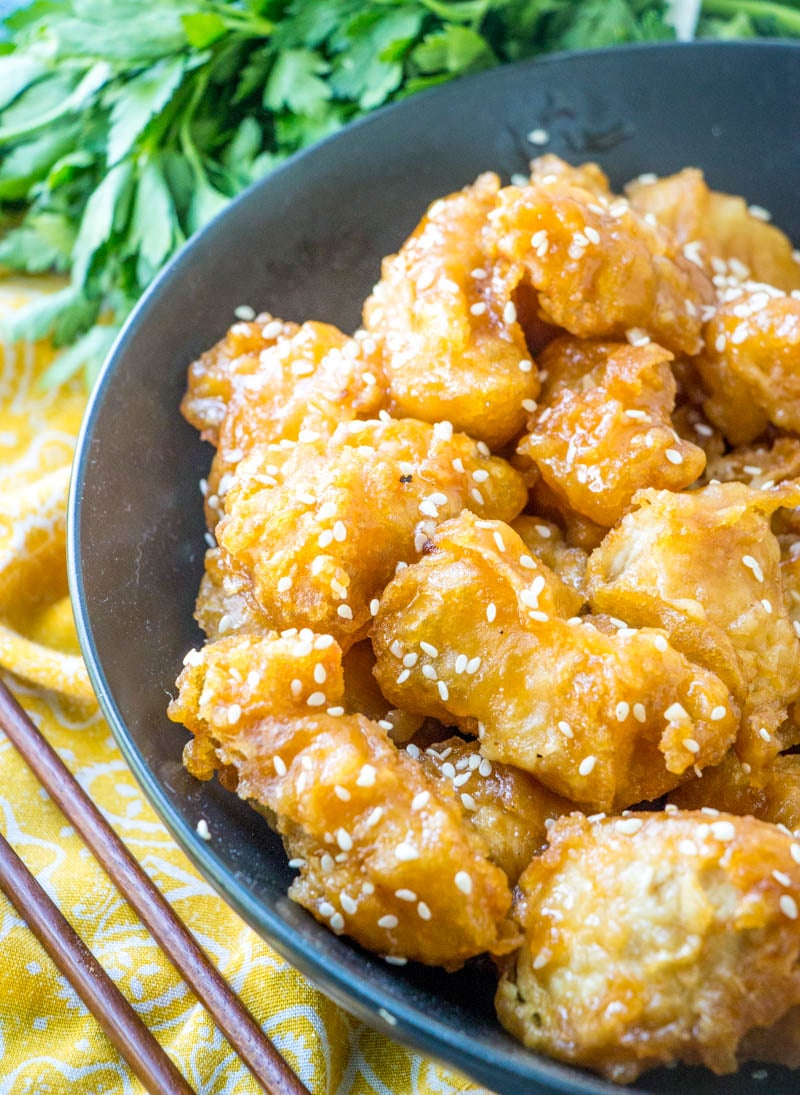 Asian style crispy honey chicken served in a black bowl with fresh green herbs in the background