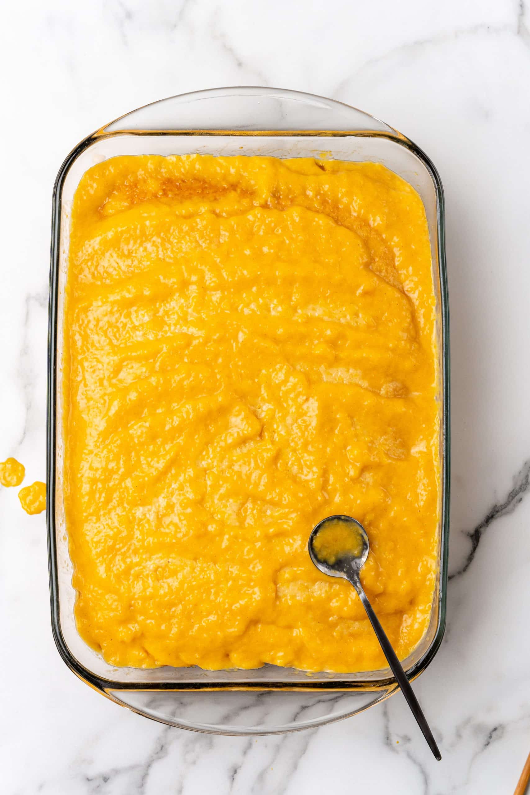 peach puree spread over a baked cake in a glass baking dish