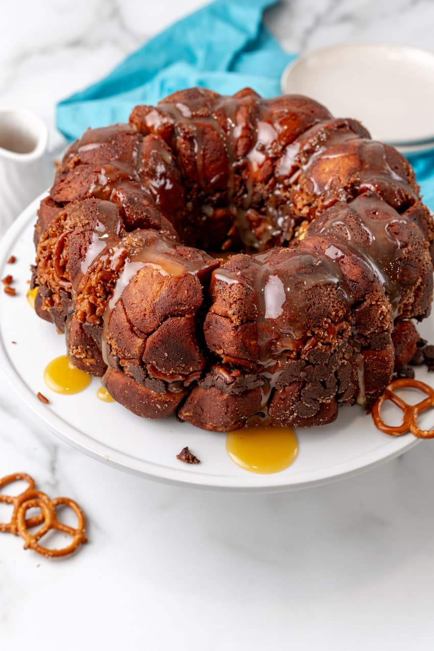 caramel drizzled overtop chocolate monkey bread sitting  on a white cake stand