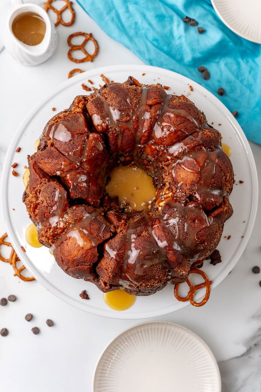 caramel drizzled overtop chocolate monkey bread sitting  on a white cake stand