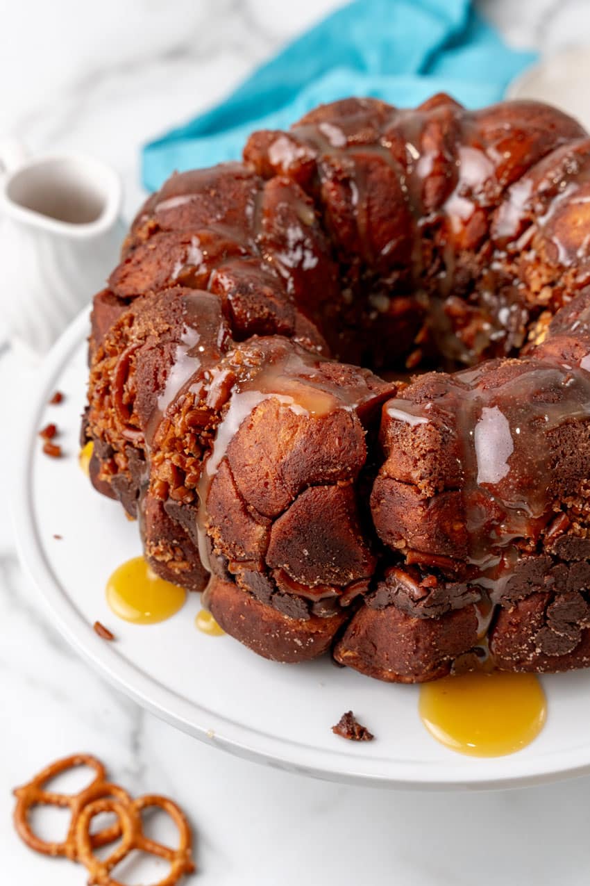 caramel drizzled overtop chocolate monkey bread sitting  on a white cake stand