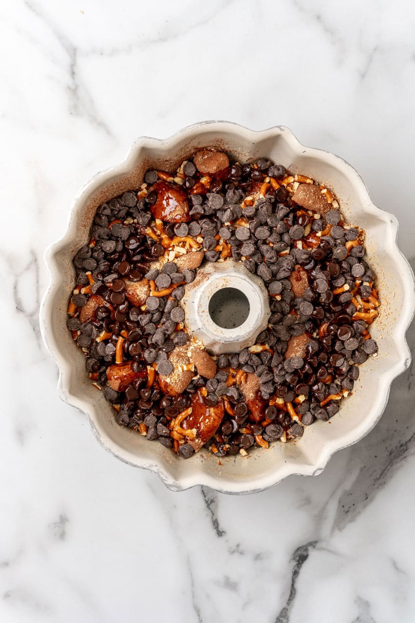 chocolate monkey bread biscuit pieces topped with pretzel pieces and chocolate chips in a white bundt pan