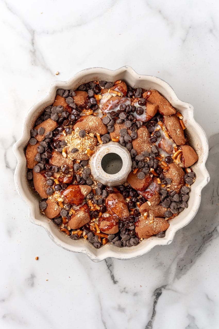 chocolate monkey bread biscuit pieces topped with pretzel pieces and chocolate chips in a white bundt pan