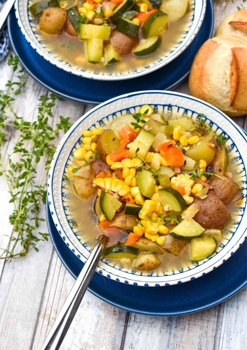 a silver spoon resting in a white bowl filled with an easy zucchini corn soup recipe