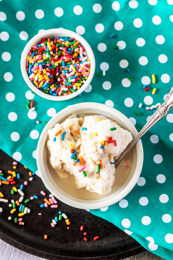 melting 5 Minute Ice Cream In A Bag served in a white ramekin with a metal spoon, and multicolored sprinkles in the background