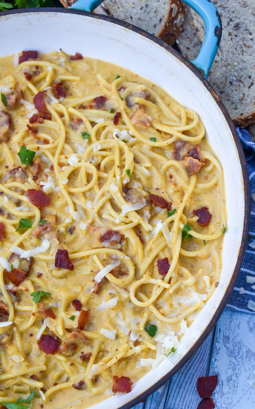 creamy pumpkin pasta topped with bacon in a blue skillet