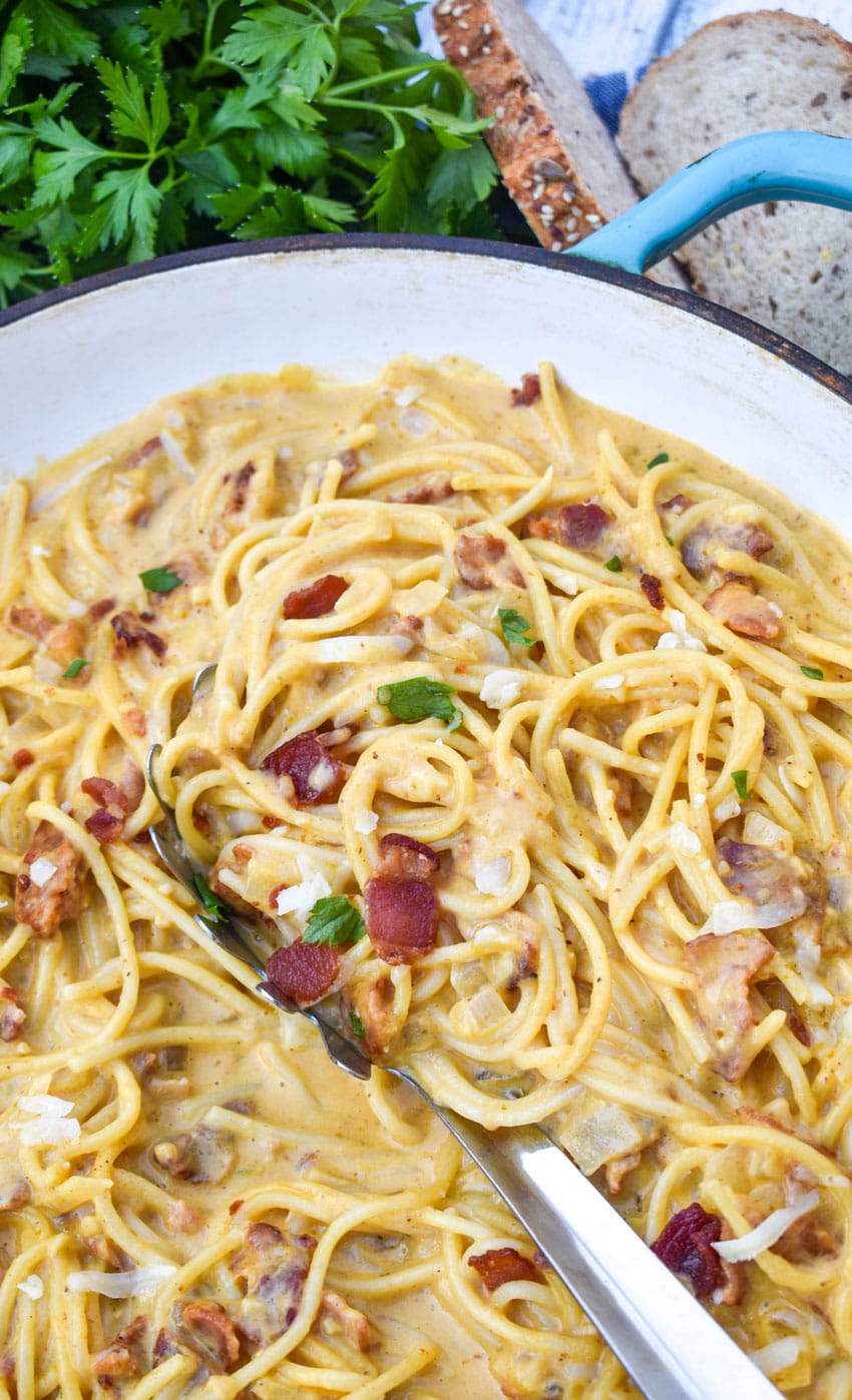 a silver spoon scooping creamy pumpkin pasta with bacon out of a blue skillet