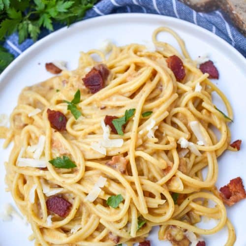 creamy one pot pumpkin pasta topped with bacon, shredded white cheddar, and fresh herbs on a white dinner plate