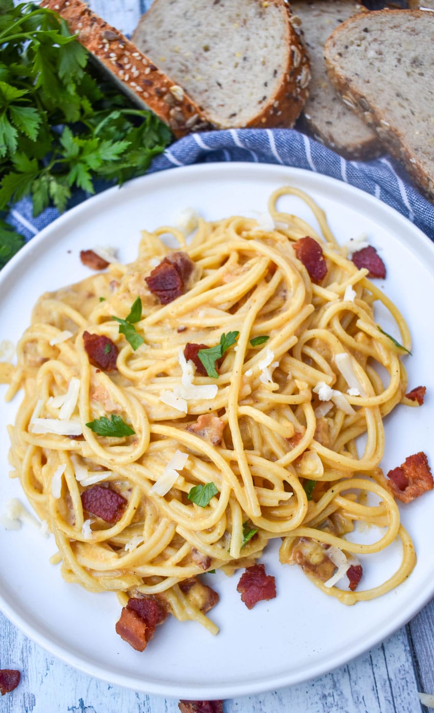 creamy one pot pumpkin pasta topped with bacon, shredded white cheddar, and fresh herbs on a white dinner plate