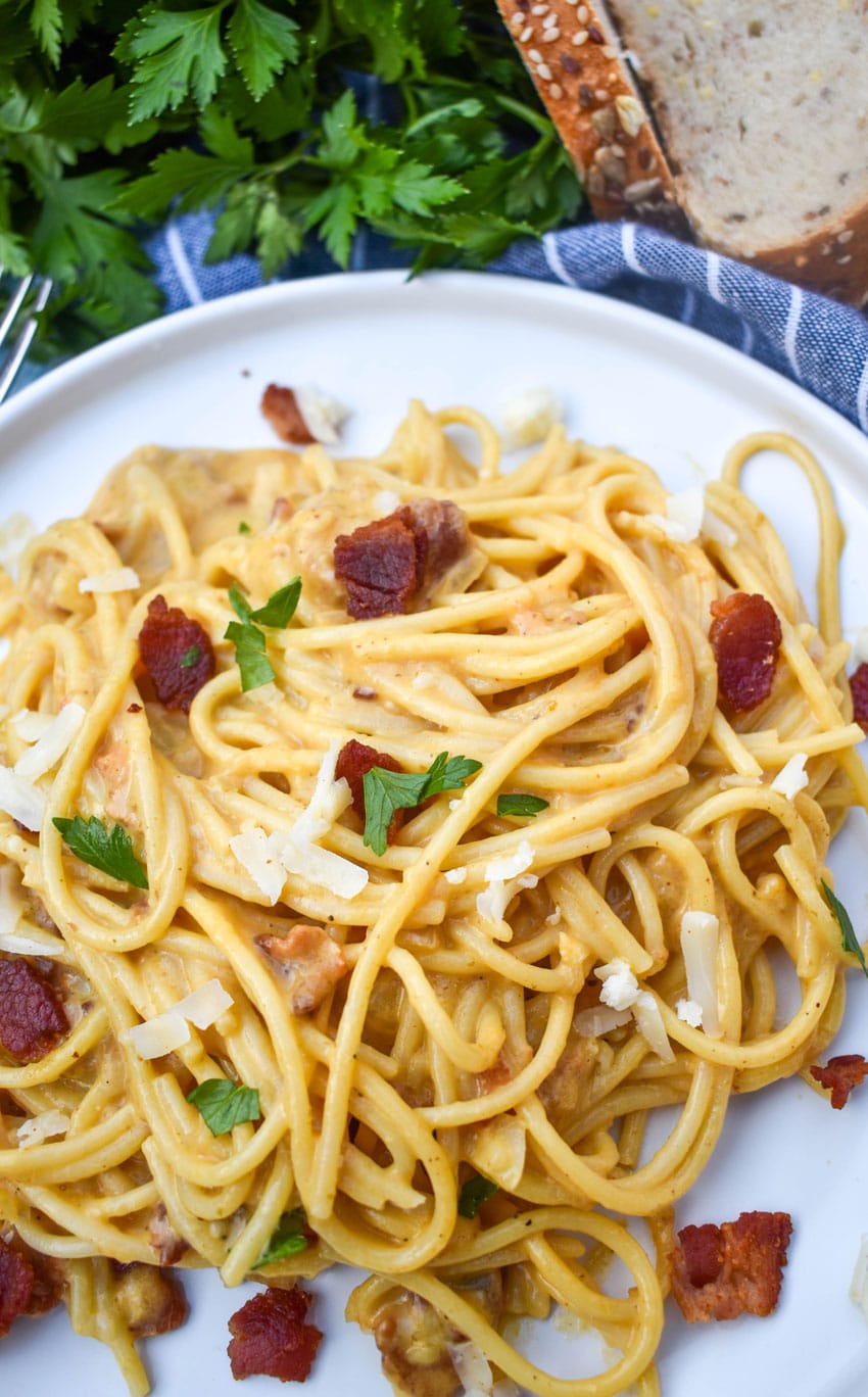 creamy one pot pumpkin pasta topped with bacon, shredded white cheddar, and fresh herbs on a white dinner plate