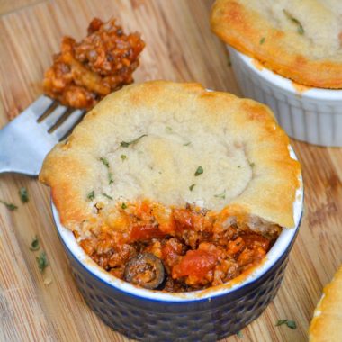 A PIZZA POT PIE IN A SMALL BLUE RAMEKIN ON A WOODEN CUTTIN GBOARD