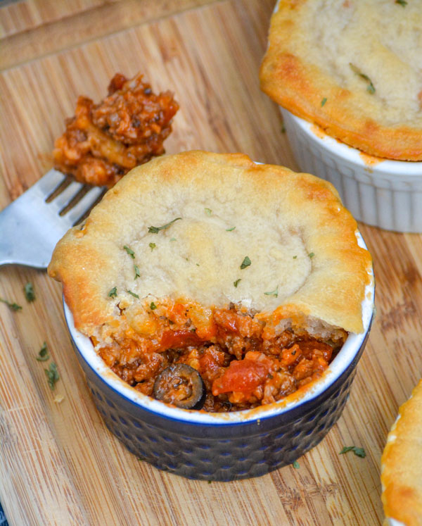 A PIZZA POT PIE IN A SMALL BLUE RAMEKIN ON A WOODEN CUTTIN GBOARD