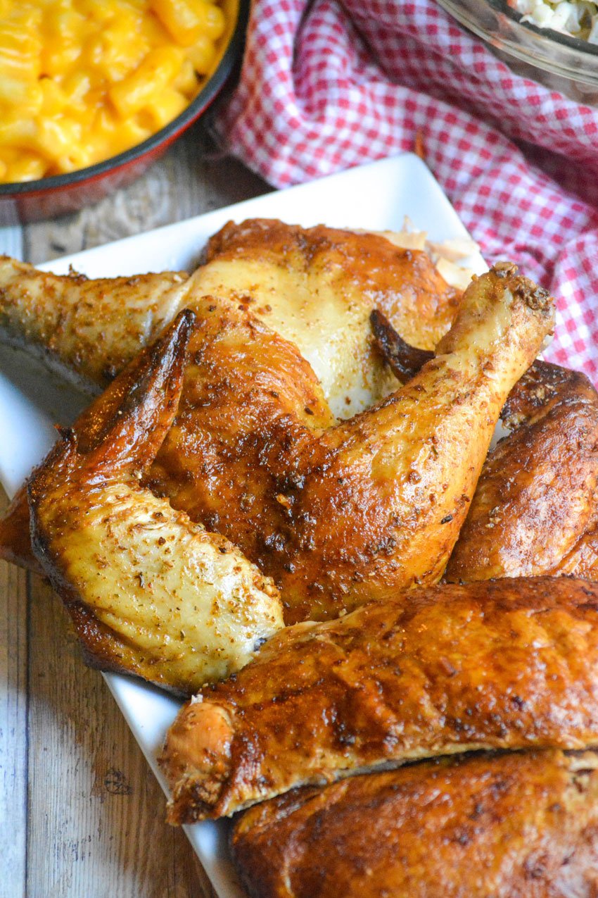 pieces of smoked beer can chicken on a white platter in front of barbecue style side dishes