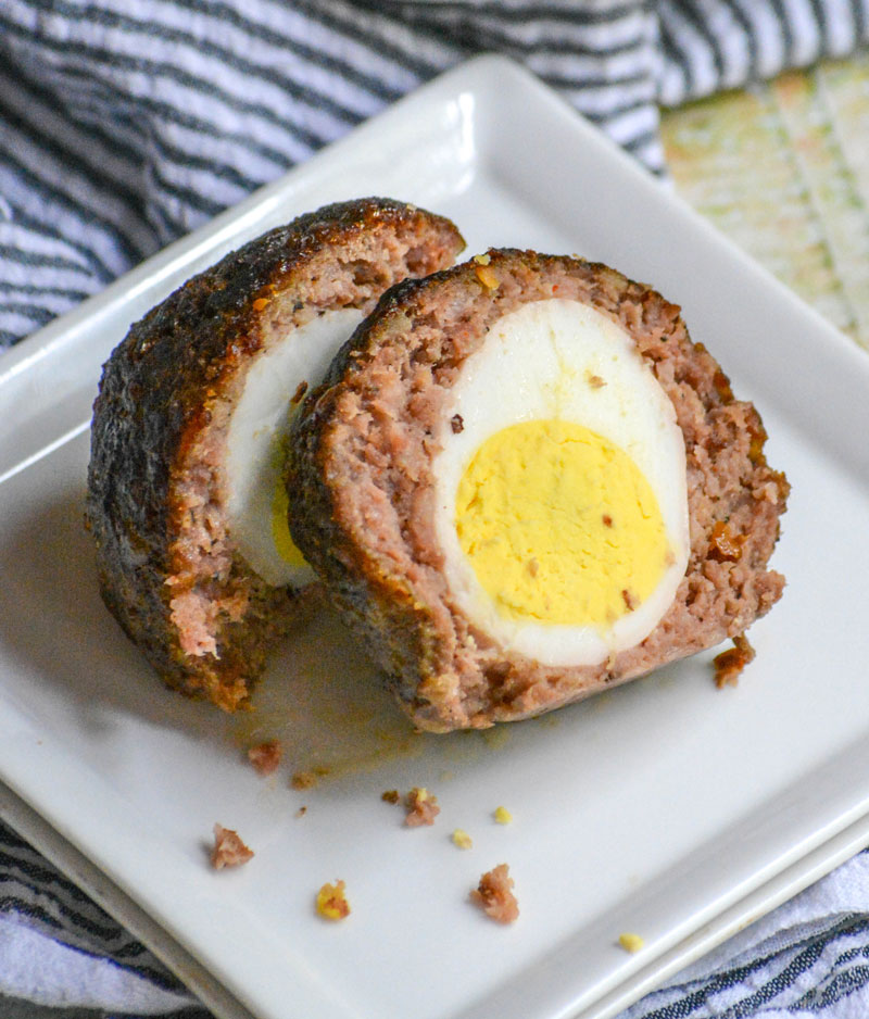 TWO HALVES OF A SMOKED SCOTCH EGG ON A SMALL WHITE APPETIZER PLATE