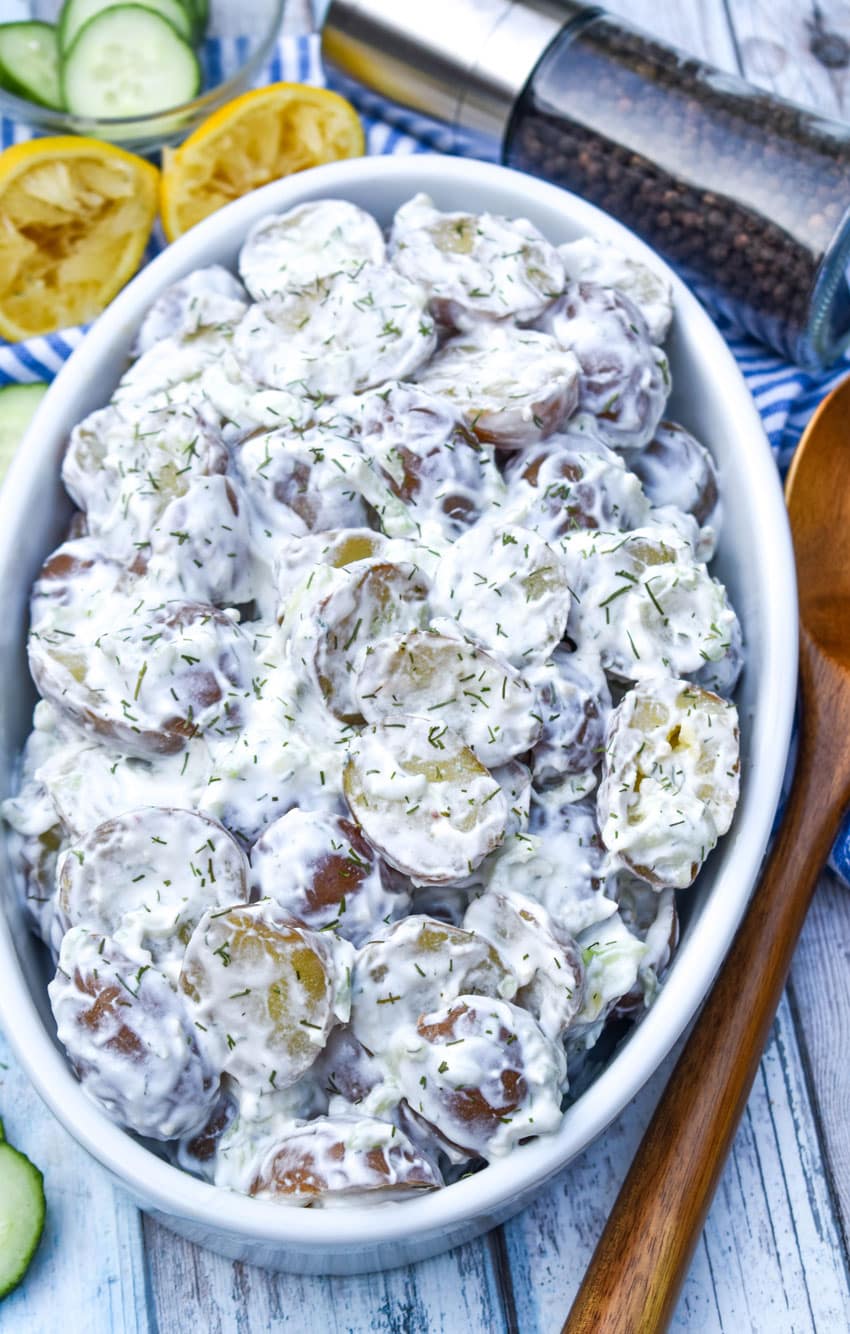 tzatziki potato salad in a white serving dish with slices of cucumber and lemon on the side