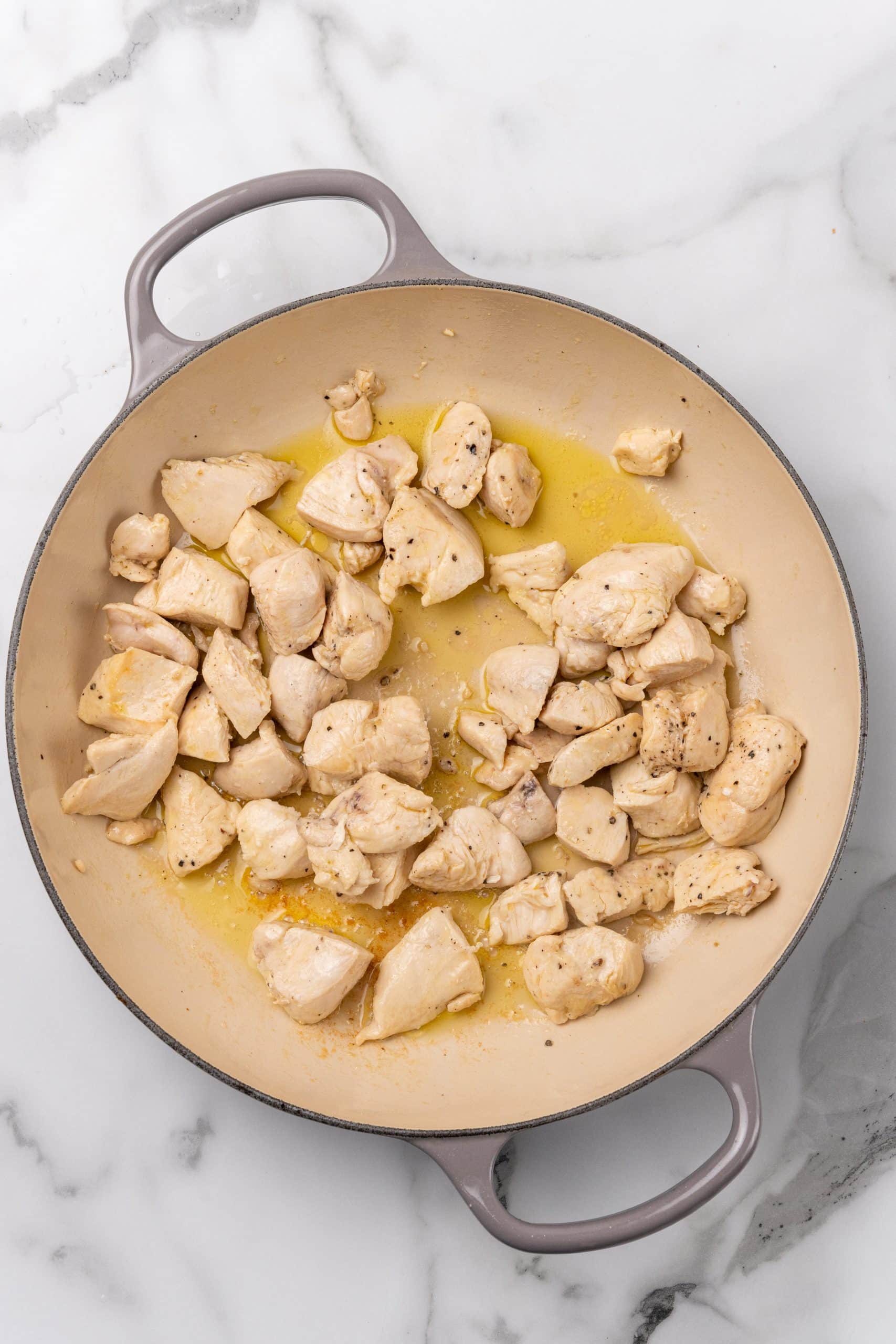 cooked chunks of chicken and olive oil in a gray skillet