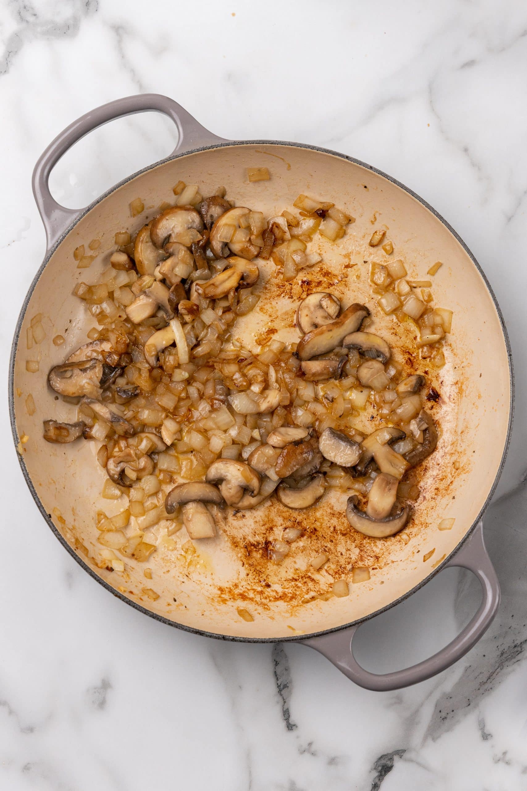 caramelized onions and sliced mushrooms in the bottom of a gray skillet