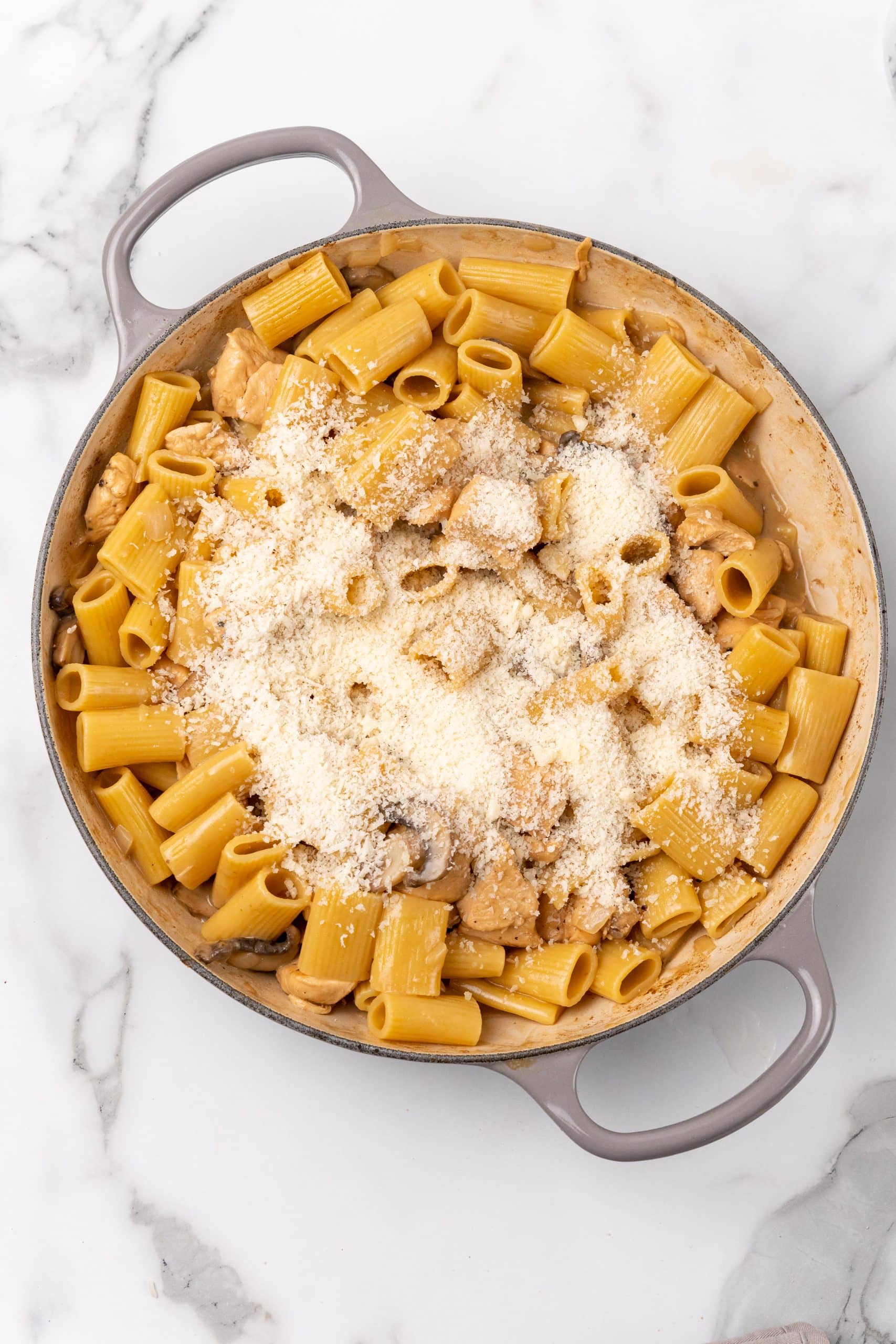 grated Parmesan cheese over chicken marsala pasta in a gray skillet
