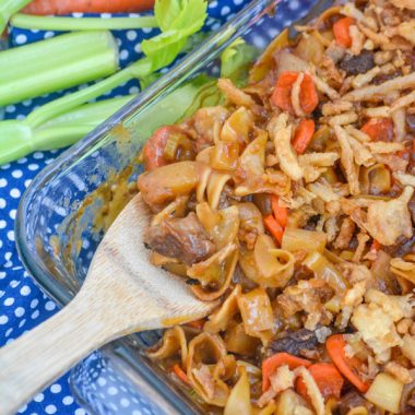 a wooden spoon stuck in a glass baking dish filled with beef noodle casserole