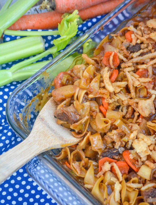 a wooden spoon stuck in a glass baking dish filled with beef noodle casserole