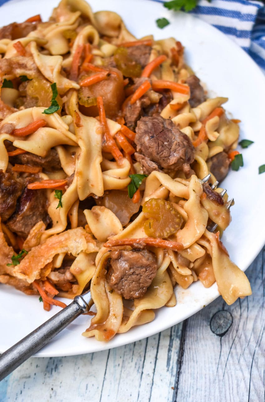 beef stew noodle casserole on a white plate with a silver fork resting on the side