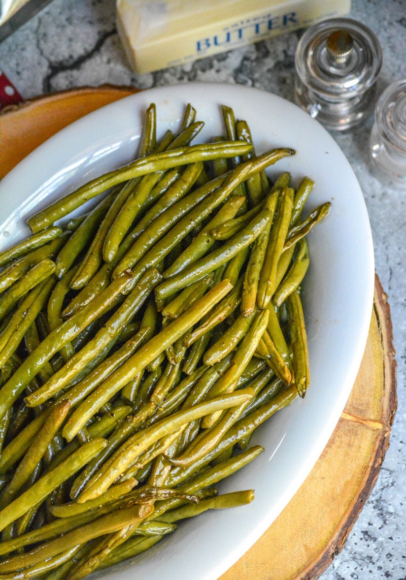 BUTTER BRAISED SMOKED GREEN BEANS IN A WHITE SERVING DISH SITTING ON A WOODEN CUTTING BOARD