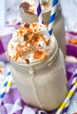 whipped cream topped butterfinger milkshake in a glass jar with paper straws on the side