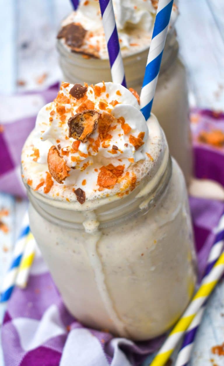 whipped cream topped butterfinger milkshake in a glass jar with paper straws on the side