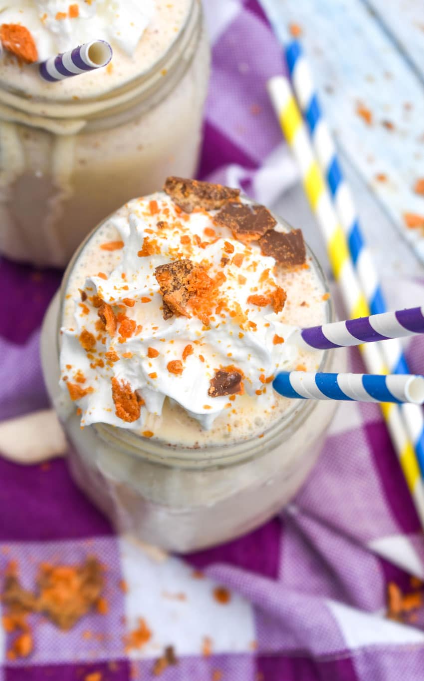 whipped cream topped butterfinger milkshake in a glass jar with paper straws on the side