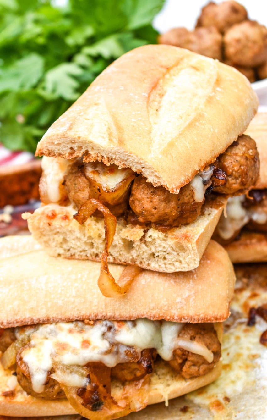 two french onion meatball sub sandwiches stacked on top of each other on a metal sheet pan
