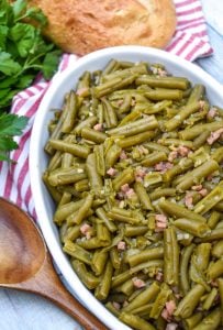 grandma's canned green beans recipe in a white serving bowl with a wooden spoon on the side