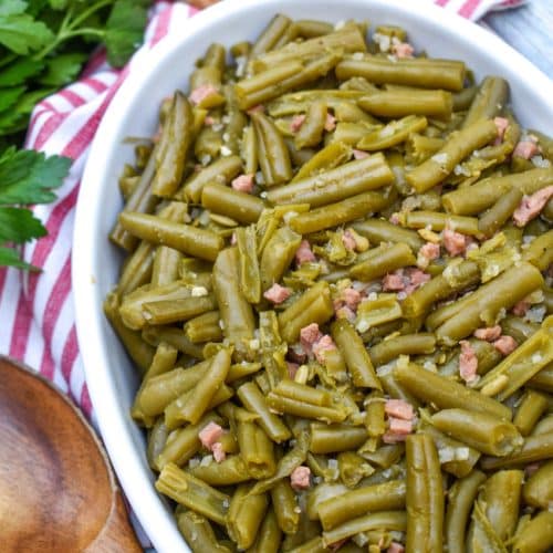 grandma's canned green beans recipe in a white serving bowl with a wooden spoon on the side