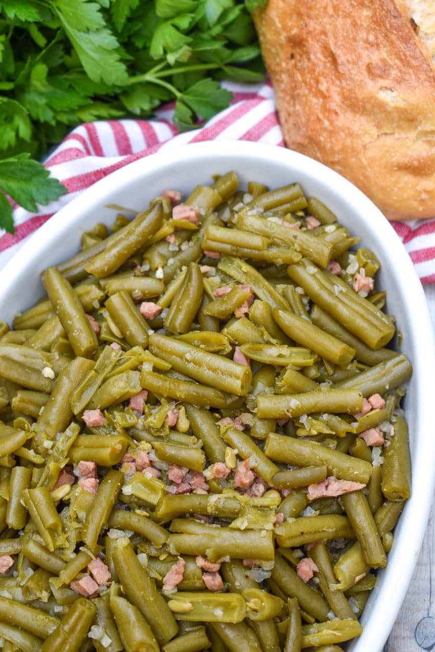 grandma's canned green beans recipe in a white serving bowl with a wooden spoon on the side