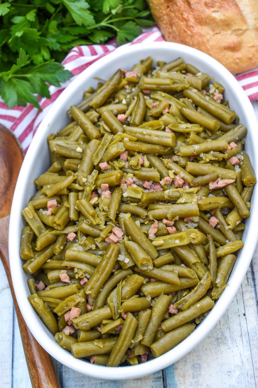 grandma's canned green beans recipe in a white serving bowl with a wooden spoon on the side