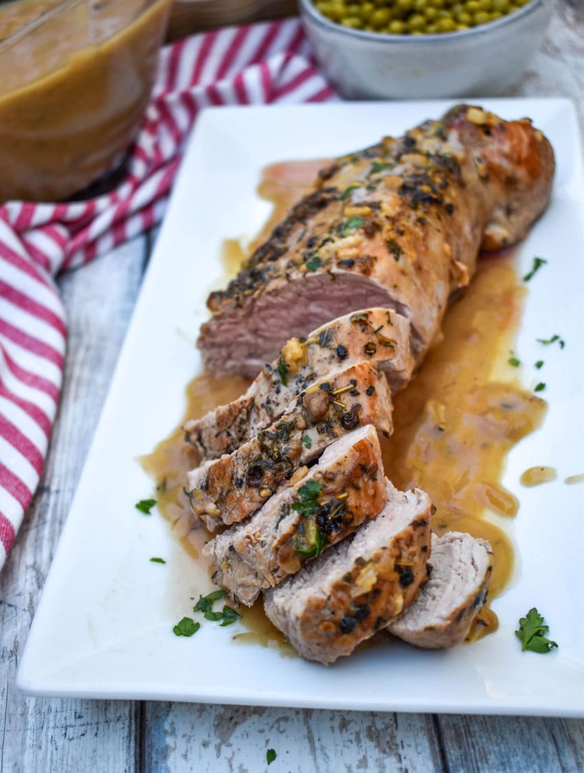 a roasted pork tenderloin smothered in apple cider gravy on a white serving platter