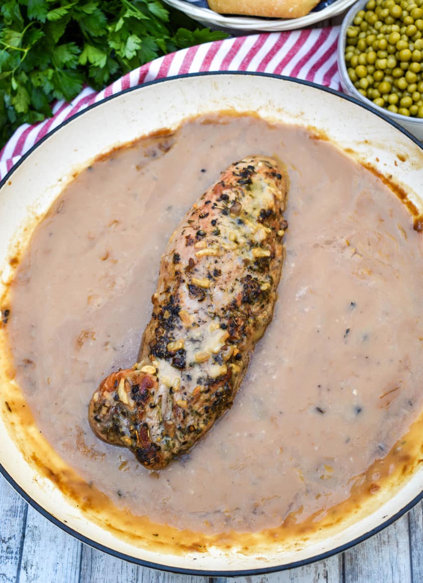 a roasted pork tenderloin in apple cider gravy in a cast iron skillet