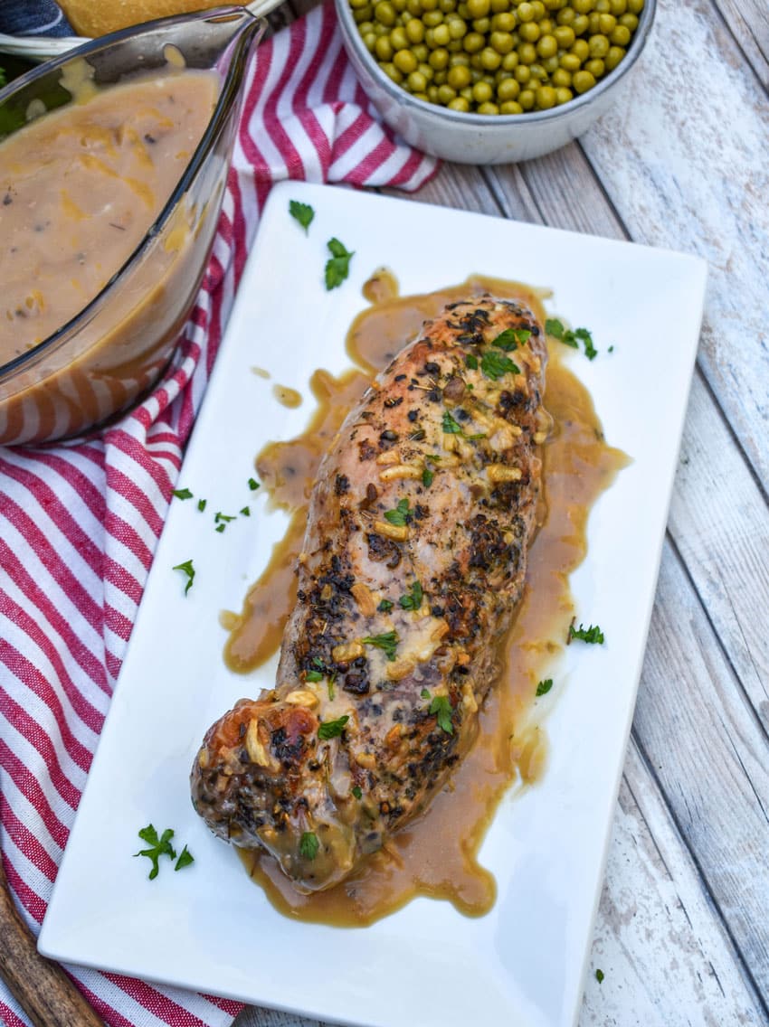 a roasted pork tenderloin smothered in apple cider gravy on a white serving platter