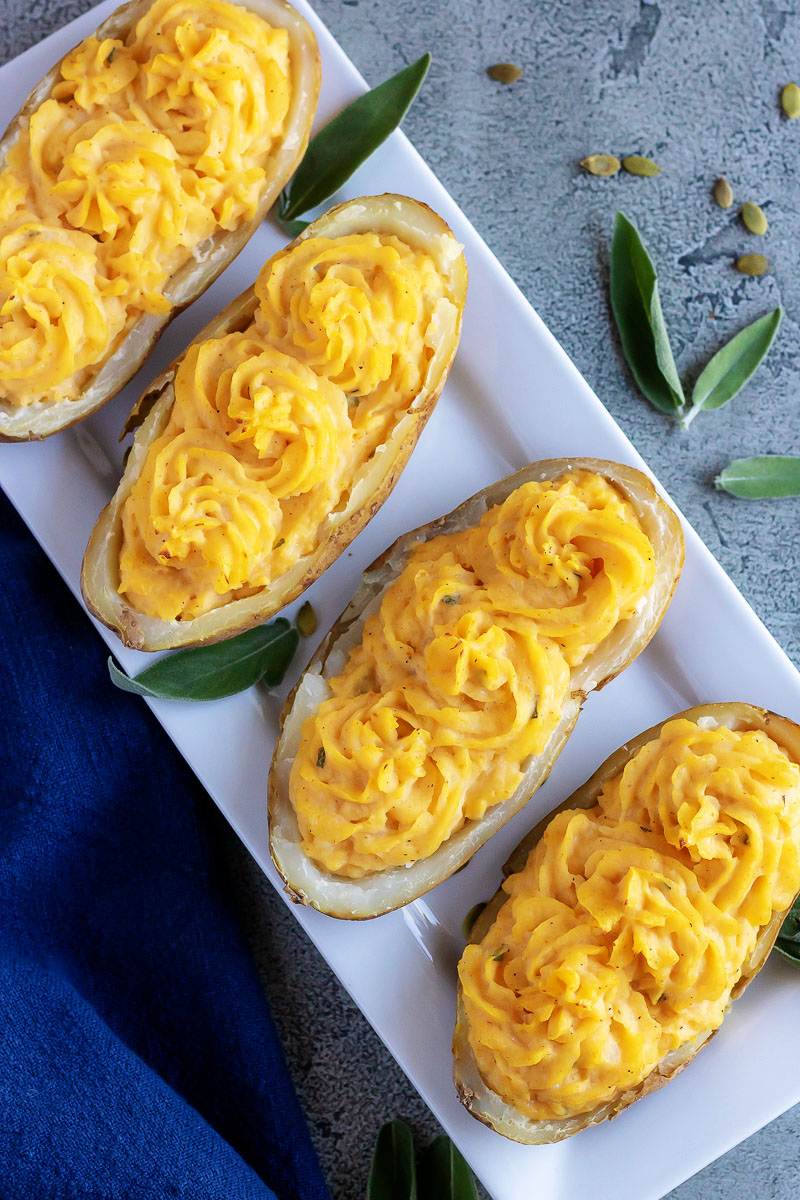 FOUR PUMPKIN PARMESAN TWICE BAKED POTATOES ON A WHITE SERVING PLATTER WITH FRESH SAGE LEAVES FOR GARNISH