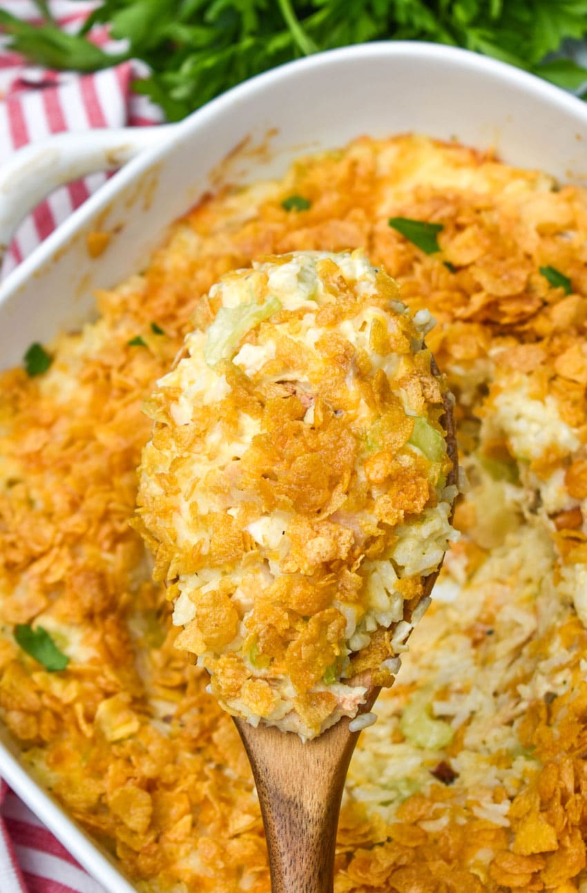 a wooden spoon lifting a scoop of rotisserie chicken and rice casserole out of a white baking dish