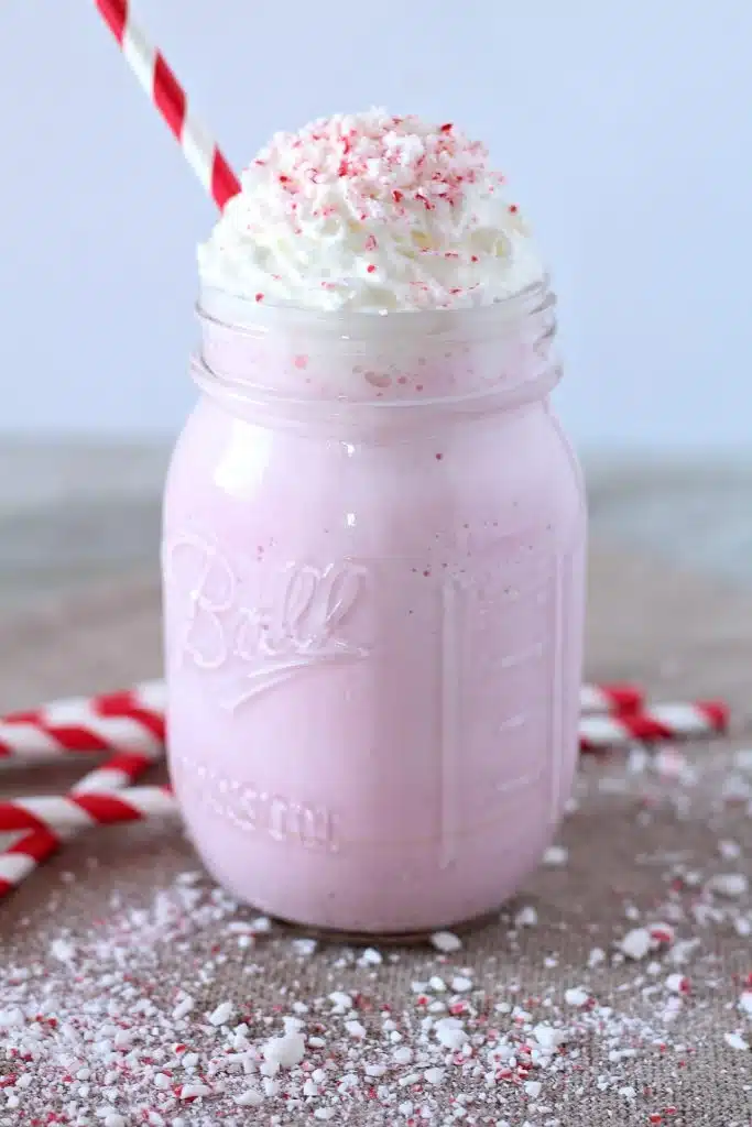 CANDY CANE MILKSHAKE IN A GLASS JAR WITH A PAPER STRAW STUCK IN FOR GARNISH