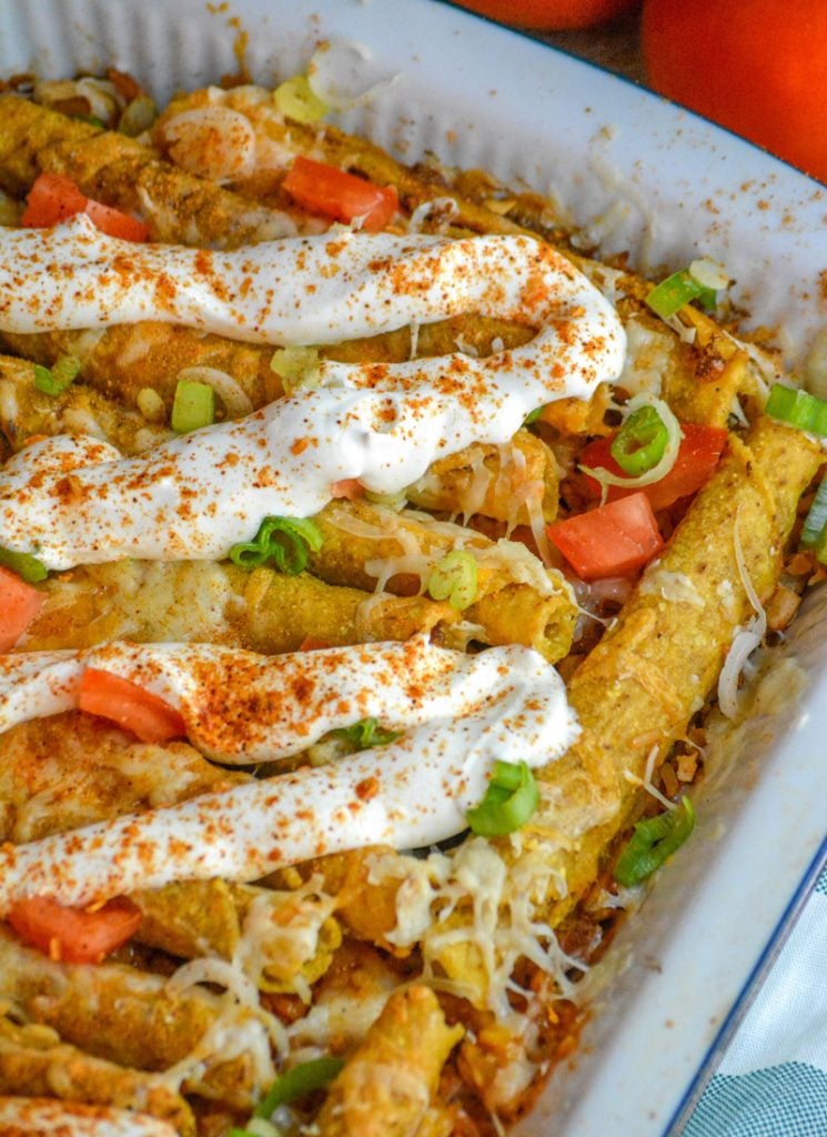 a cheesy beef taquito casserole served in a white casserole dish topped with a thick drizzle of sour cream 
