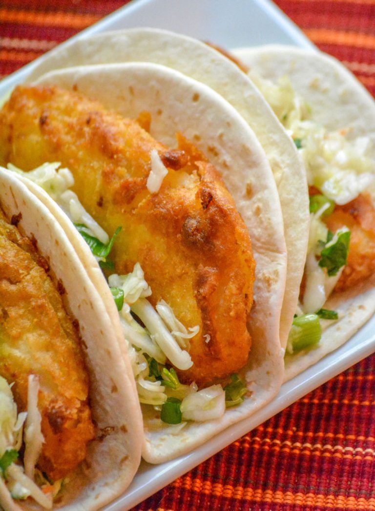 beer battered fish tacos with cilantro lime slaw arranged in a row on a white platter