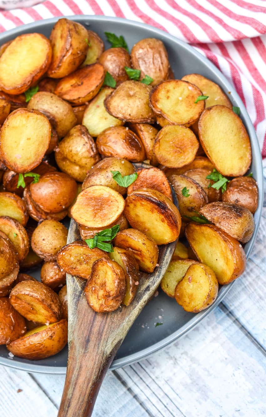 a wooden spoon scooping salt and vinegar potatoes out of a shallow gray bowl