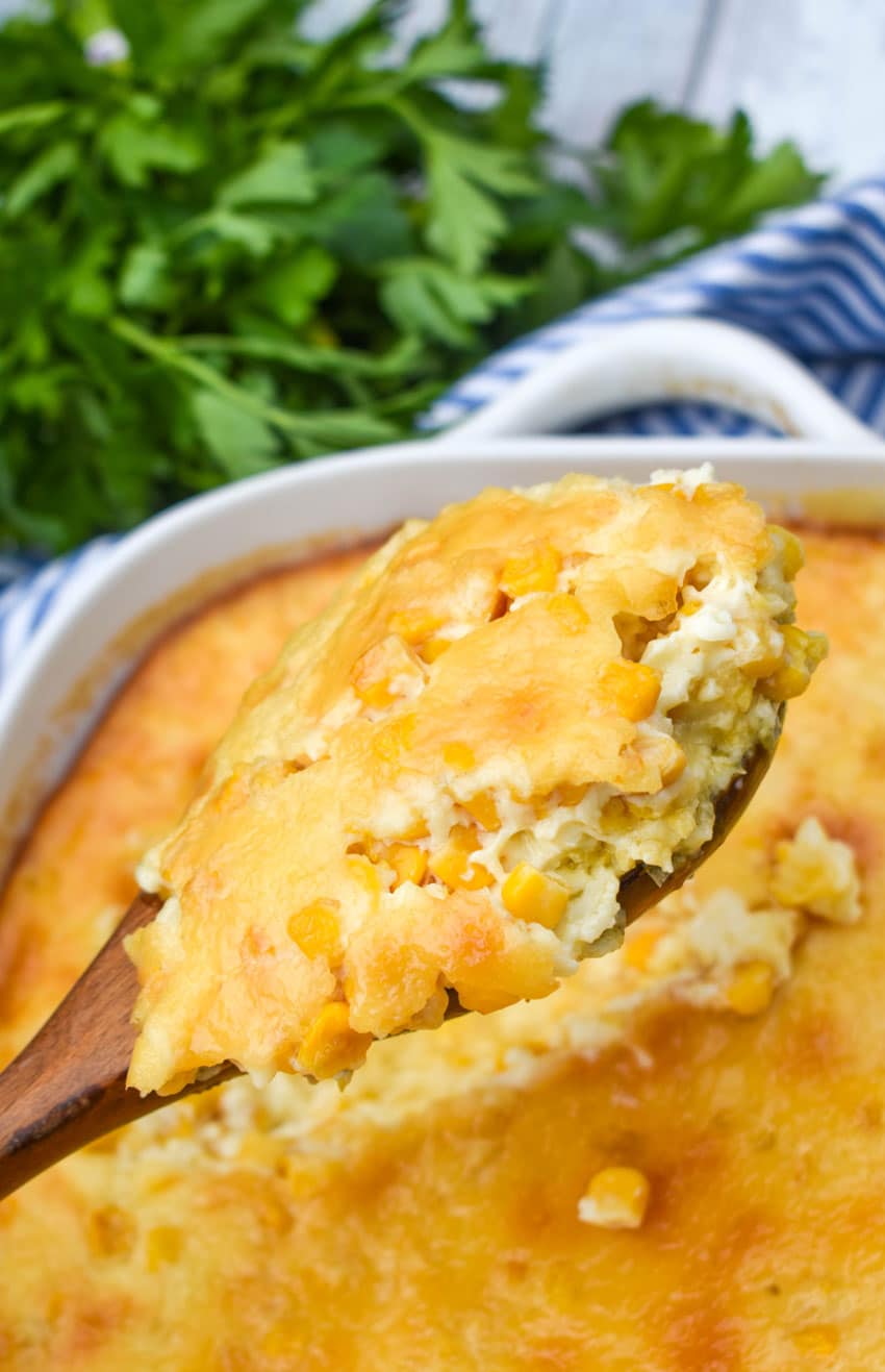 A wooden serving spoon holding up a scoop of baked Southern creamed corn pudding recipe