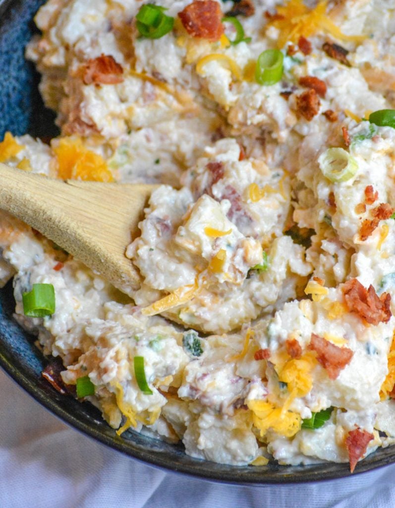 a wooden spoon stuck in a bowl of Loaded Baked Potato Salad ready to scoop