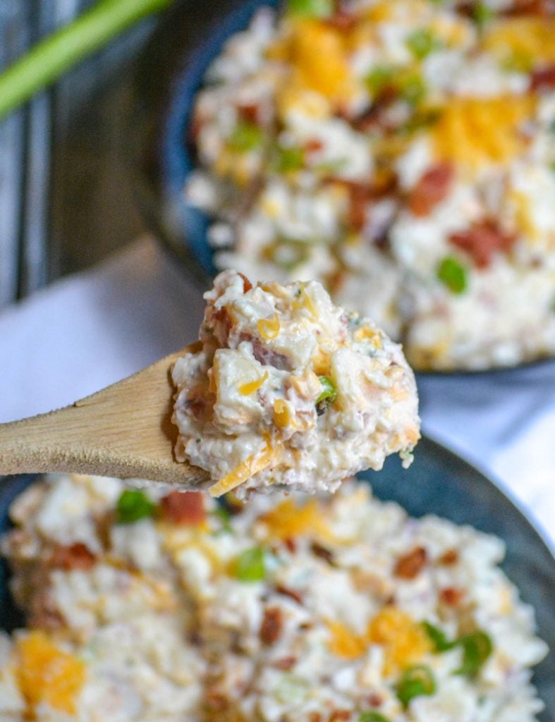 a scoop of Loaded Baked Potato Salad held aloft on a wooden spoon